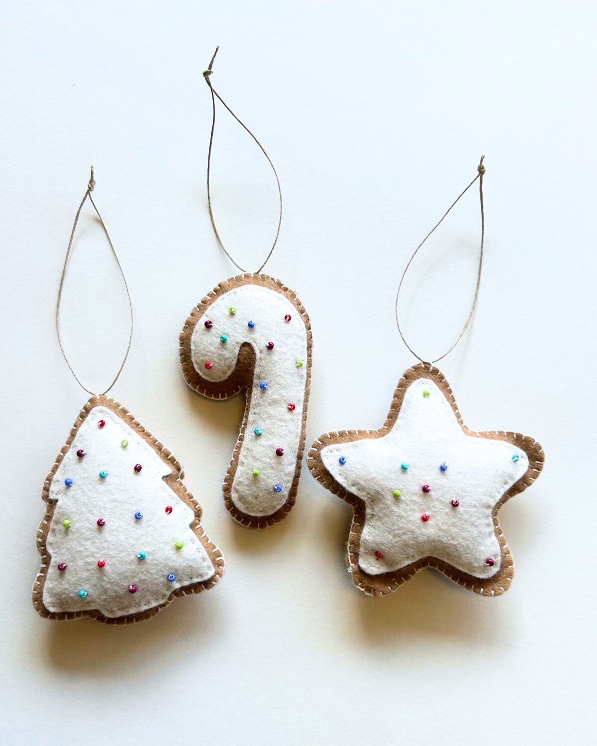 Three felt Christmas ornaments shaped like a tree, candy cane, and star on a white background.