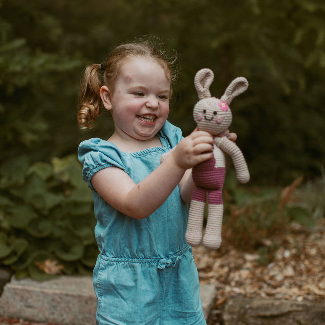 girl holding plush bunny in dark pink overalls